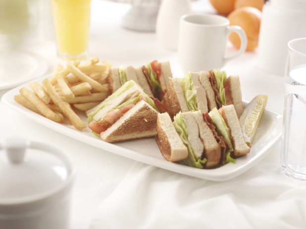 Chicken club sandwich, quartered, with french fries, on a square white plate in an all-white table setting