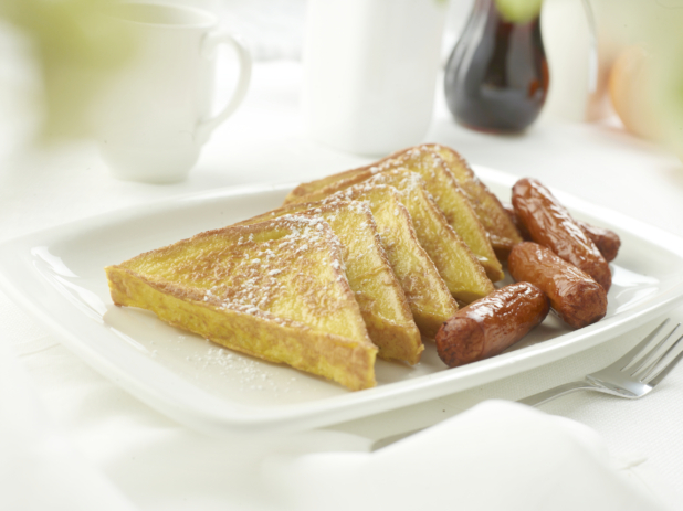 French toast with breakfast sausages on a square white plate in an all-white table setting