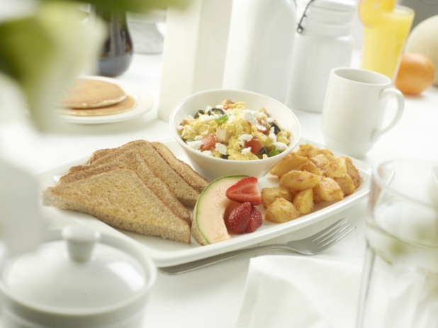 Mediterranean-style scrambled eggs with feta cheese, black olives, tomatoes, and green onion with homefries, fruit, and brown toast in a white table setting