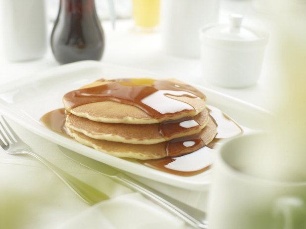 A Stack of Buttermilk Pancakes with Maple Syrup in a White Platter on a White Table Cloth Surface in a Restaurant Setting