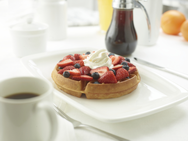 Belgian waffle with fresh strawberries and blueberries topped with whipped cream in an all-white table setting