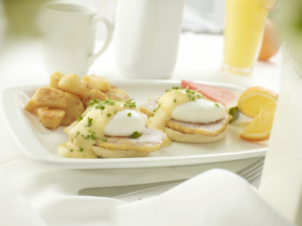 Classic Eggs Benedict with homefries and fresh fruit in an all-white setting, white background