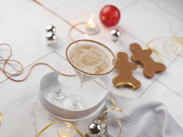 Eggnog martini on a white tabletop with gingerbread men and silver, red, and gold Christmas decorations