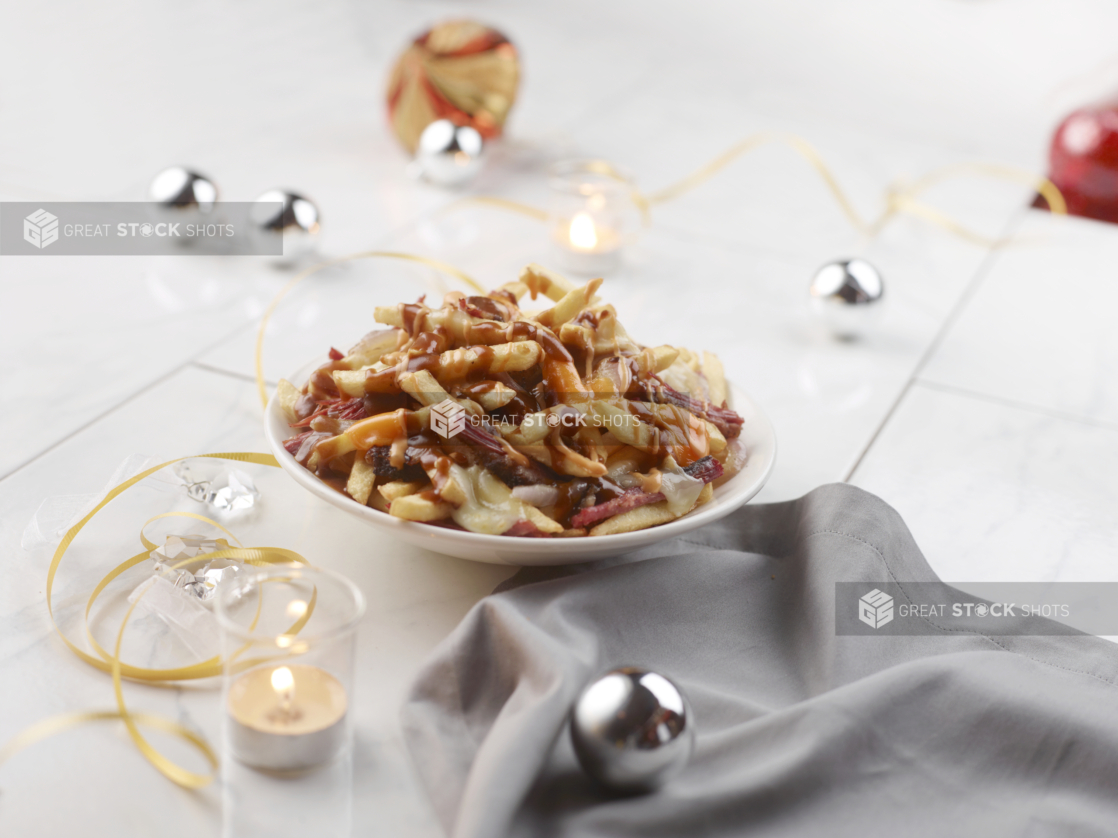 Poutine in a white bowl on a table with gold, silver, and red Christmas decorations