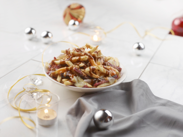 Poutine in a white bowl on a table with gold, silver, and red Christmas decorations