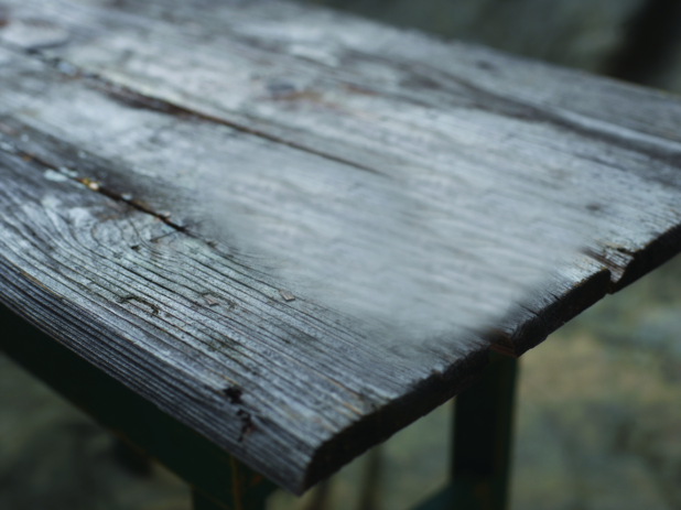 Close Up of a Weathered Wooden Table End Against a Brown Canvas Background