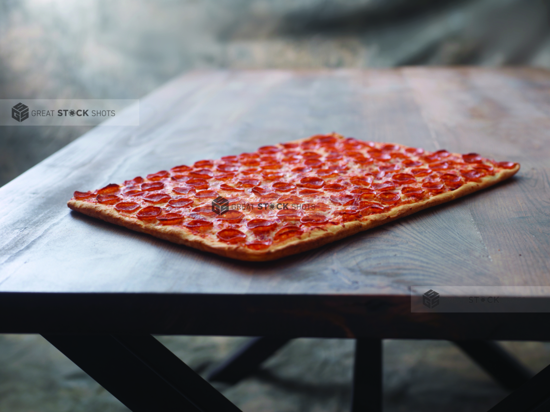 A Large Party-sized Pepperoni Pizza on a Dark Wooden Table Against a Brown Canvas Background