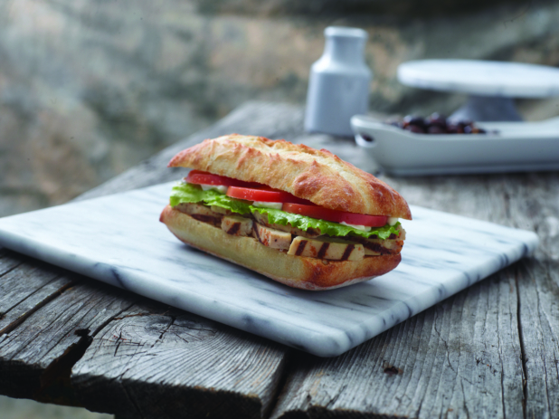 Italian Sandwich with Grilled Chicken Strips and Fresh Vegetables in a Toasted Ciabatta Bun on a Marble Cutting Board on an Aged Wooden Table