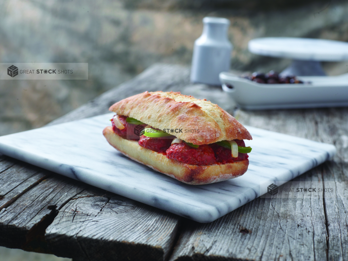 Italian Sandwich with Sautéed Veggies and Meatball Halves Smothered in Marinara Sauce in a Toasted Ciabatta Bun on a Marble Cutting Board on an Aged Wooden Table