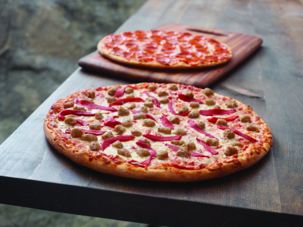 A Pizza with Roasted Red Peppers and Italian Sausage and a Pepperoni Pizza on a Wooden Cutting Board on a Dark Wood Table Against a Brown Canvas Background