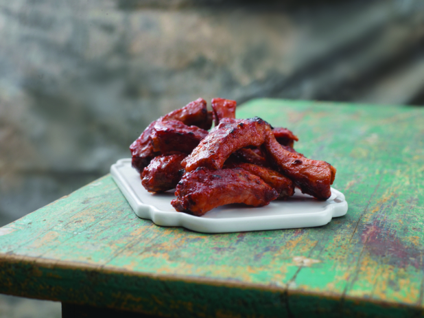 A Close Up of a Dish of a Full Rack of BBQ Back Ribs on a Weathered Painted Wooden Table