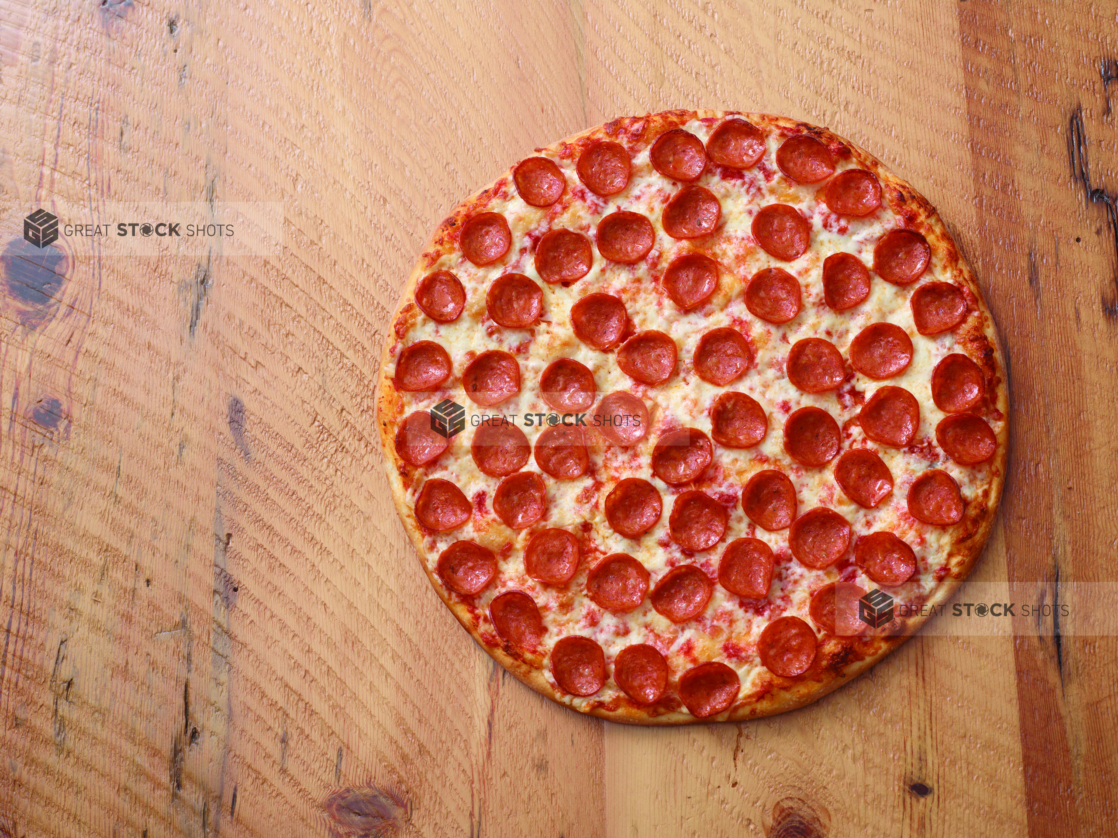 Overhead View of a Whole New York Style Pepperoni Pizza on a Two Tone Wooden Table