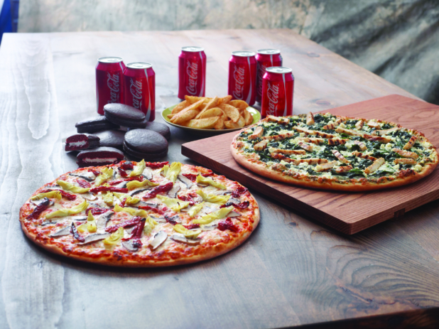 Family Pizza Special with a Chicken Florentine Pizza and a 3-Topping Vegetarian Pizza, Chocolate Cakes, Potato Wedges and a 6-Pack of Soda on a Dark Wooden Surface