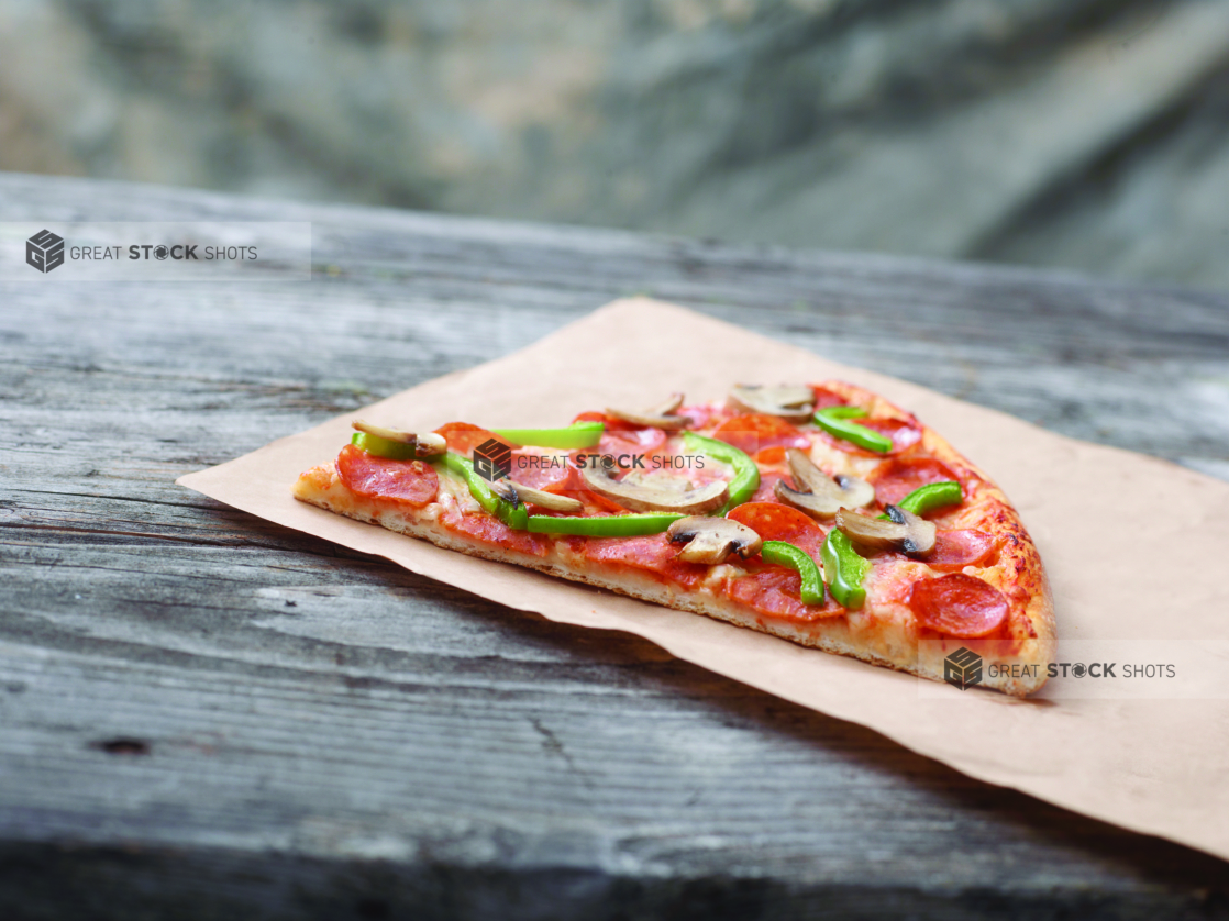 Jumbo Deluxe Pizza Slice on Kraft Paper on a Weathered Wooden Table