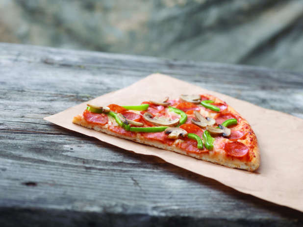Jumbo Deluxe Pizza Slice on Kraft Paper on a Weathered Wooden Table