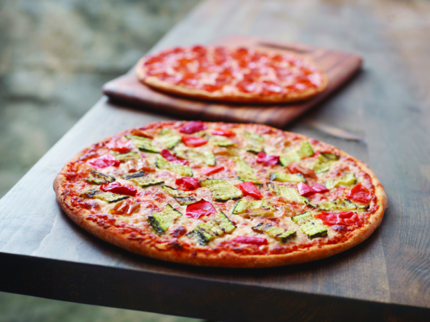 A Pizza with Grilled Zucchini and Hot Banana Peppers and a Pepperoni Pizza on a Wooden Cutting Board on a Dark Wood Table Against a Brown Canvas Background