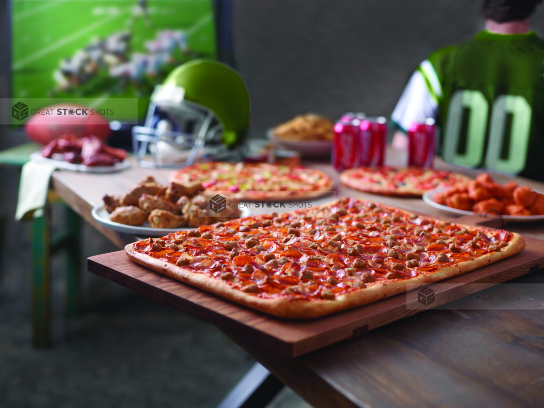 Pizza Party with a Canadian Party Pizza, Deluxe Pizza, Focaccia Bread, Boneless Wings, Roasted Italian Wings, BBQ Ribs, Potato Wedges and Cans of Coca-Cola on a Wooden Table for a Football Game Viewing Party