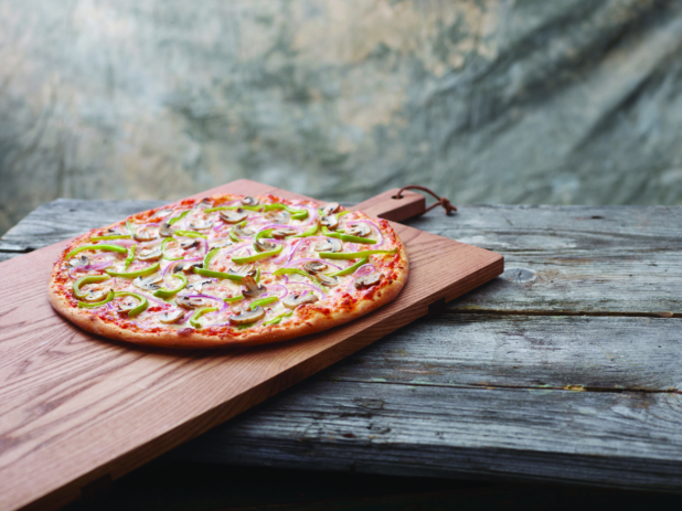 A Pizza with Green Onions, Mushrooms and Red Onions on a Wooden Cutting Board on a Aged Wooden Table Against a Brown Canvas Background