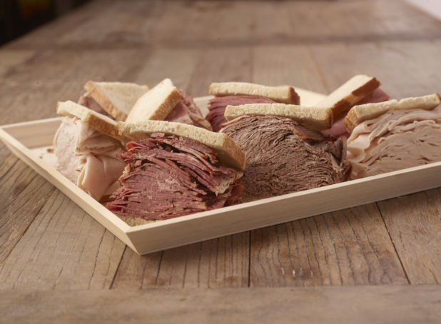 Corned beef, smoked meat, and turkey sandwiches on sliced bread on a wood serving tray