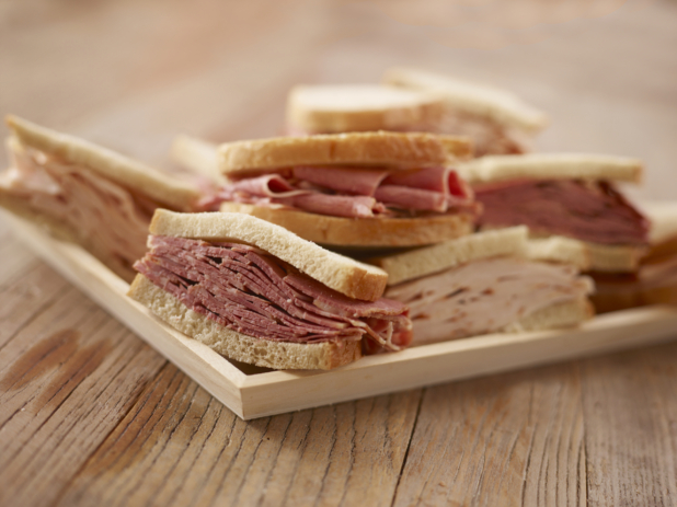 Close Up of a Wooden Catering Platter of Pastrami and Roast Turkey Sandwiches on White Rye Bread on a Weathered Wooden Surface