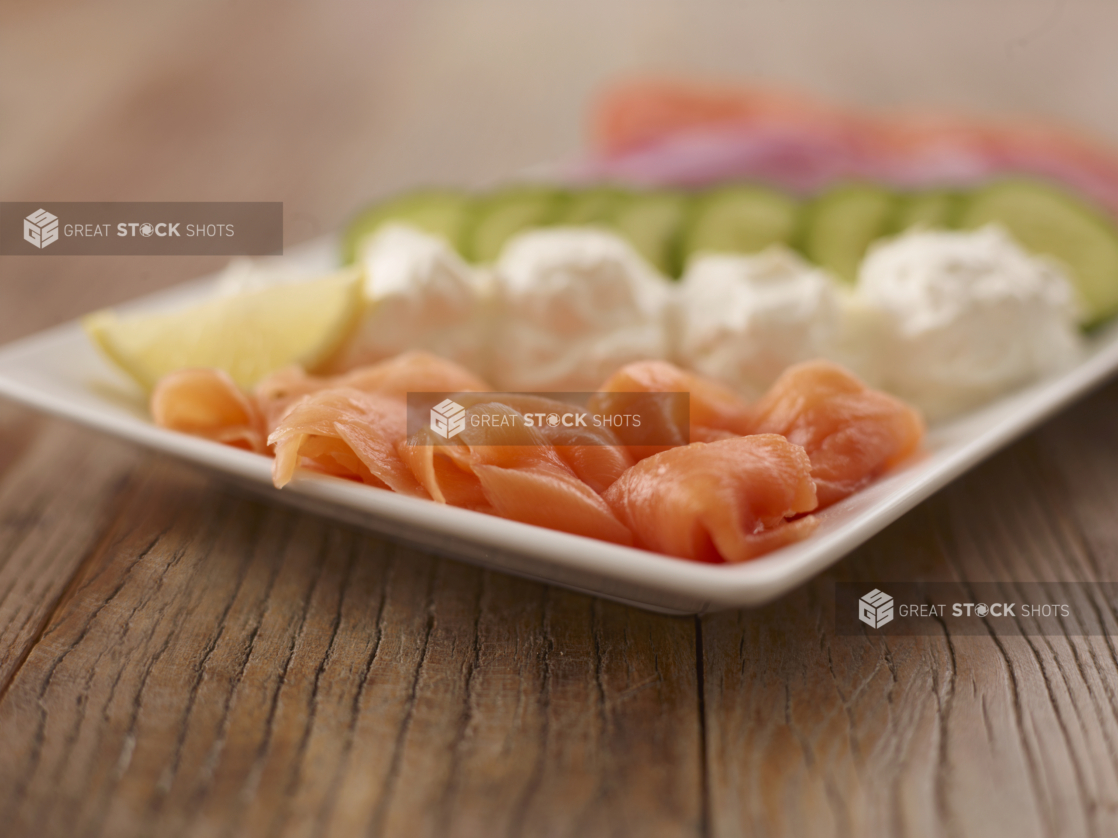 White Rectangle Platter of Smoked Salmon and Cream Cheese With Slices of Fresh Vegetables on a Wooden Surface