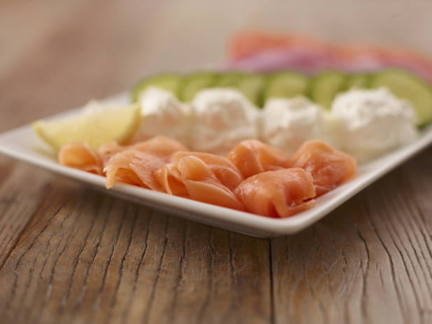 White Rectangle Platter of Smoked Salmon and Cream Cheese With Slices of Fresh Vegetables on a Wooden Surface