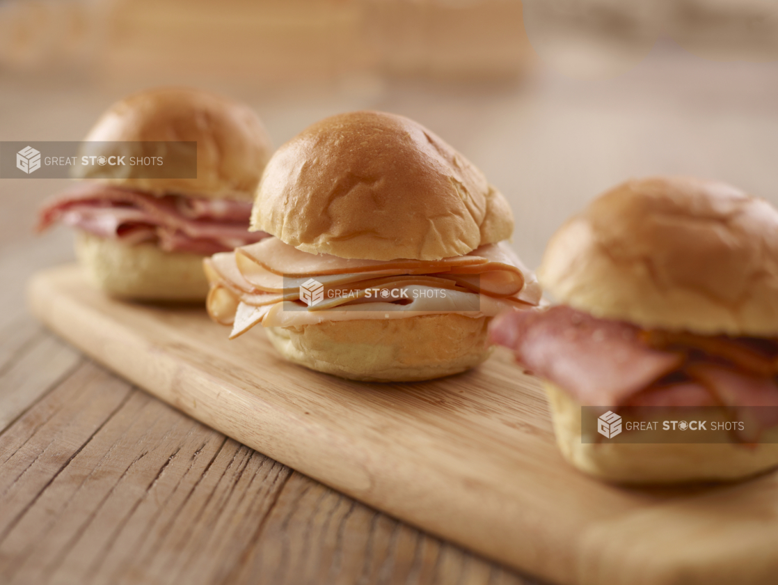 A Trio of Cold Deli Meat Sandwiches on a Wooden Cutting Board on a Wooden Table