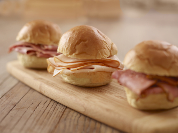 A Trio of Cold Deli Meat Sandwiches on a Wooden Cutting Board on a Wooden Table