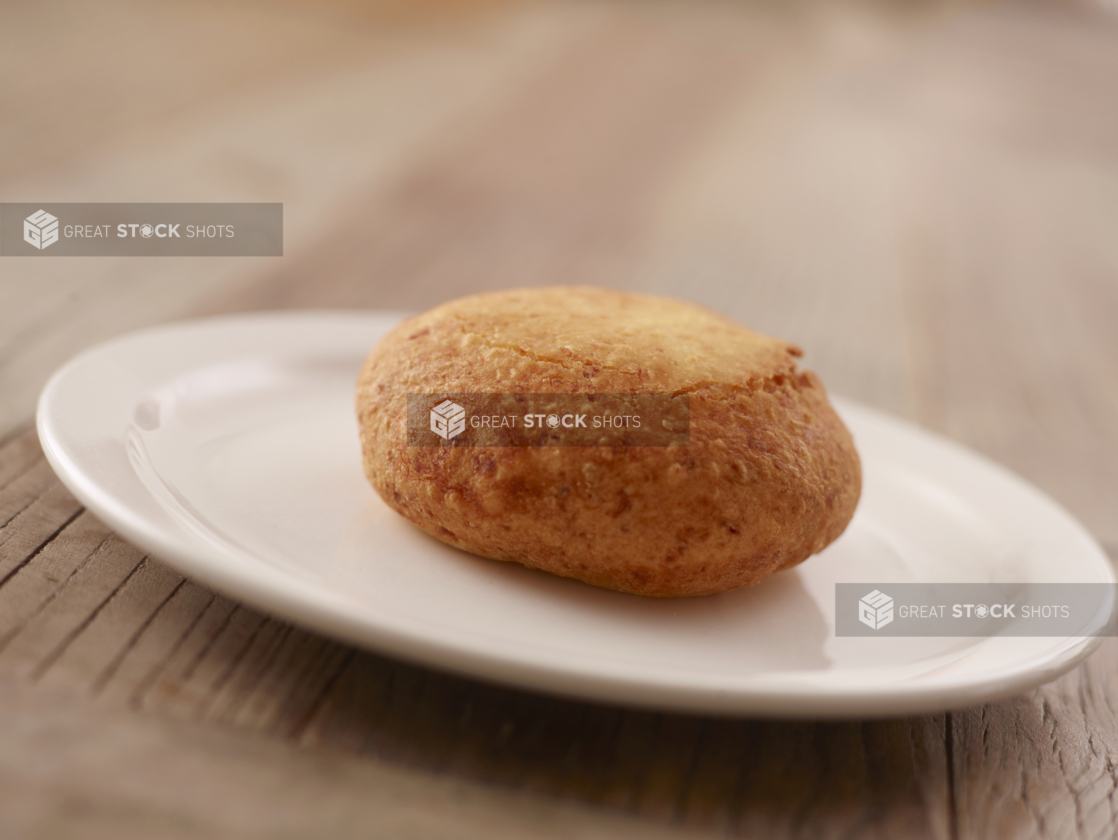 A Plain Beef Knish on a Round White Plate on a Wooden Table