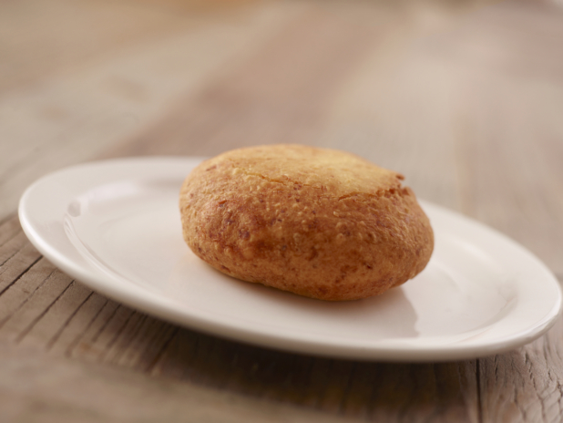 A Plain Beef Knish on a Round White Plate on a Wooden Table