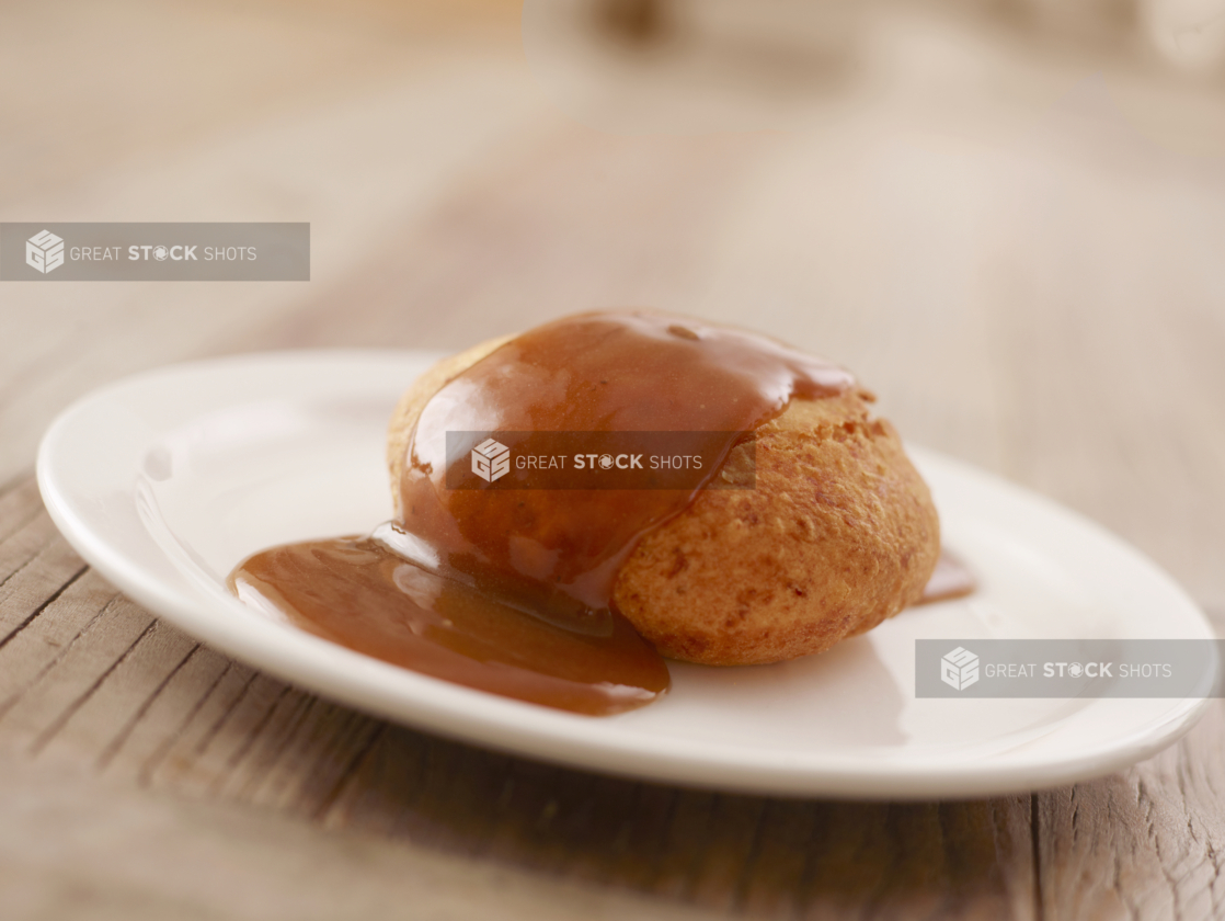 A Beef Knish Covered in Brown Gravy on a Round White Plate on a Wooden Table