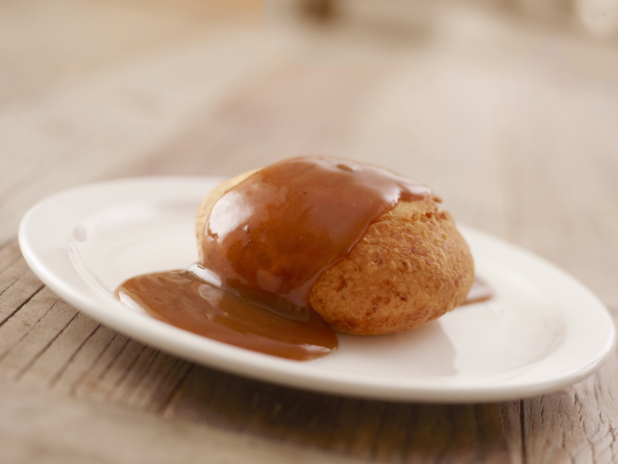 A Beef Knish Covered in Brown Gravy on a Round White Plate on a Wooden Table