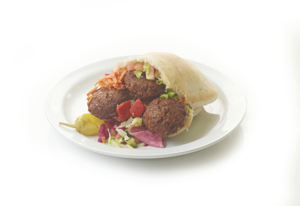 A White Pita Pocket Stuffed with Deep Fried Falafel Balls, Shredded Vegetables and Pickled Veggies with a Peppercini on a Round White Plate, Isolated on a White Background