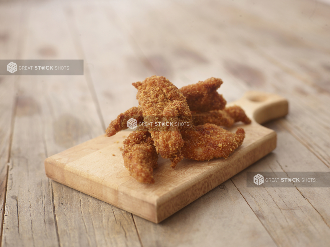 Deep Fried Breaded Chicken Tenders on a Wooden Cutting Board on a Weathered Wooden Surface