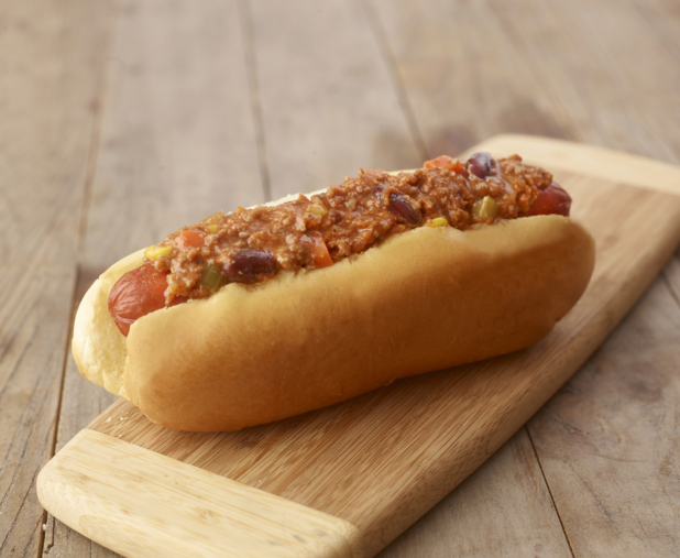 Close Up of a Chilli Hot Dog on a Small Wooden Cutting Board on a Rustic Wood Surface
