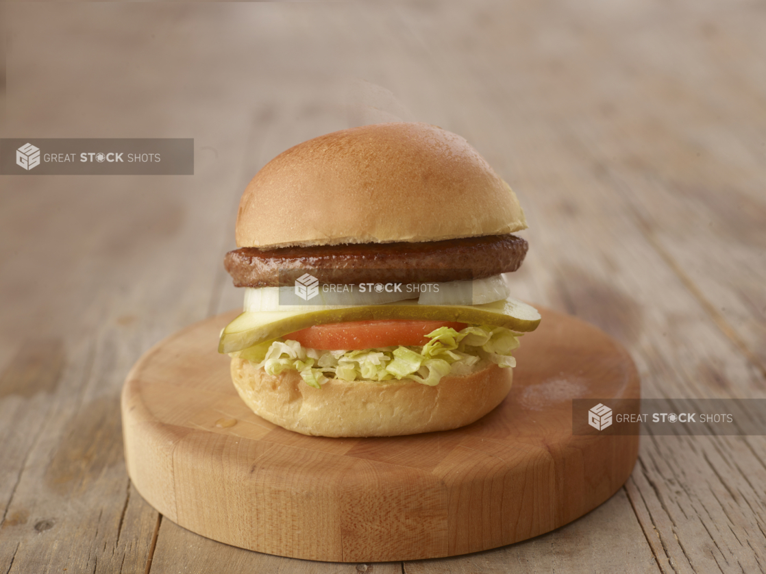 Close up of a Beef Burger with Fresh Vegetable Toppings on a Wooden Cutting Board on a Weathered Wood Surface