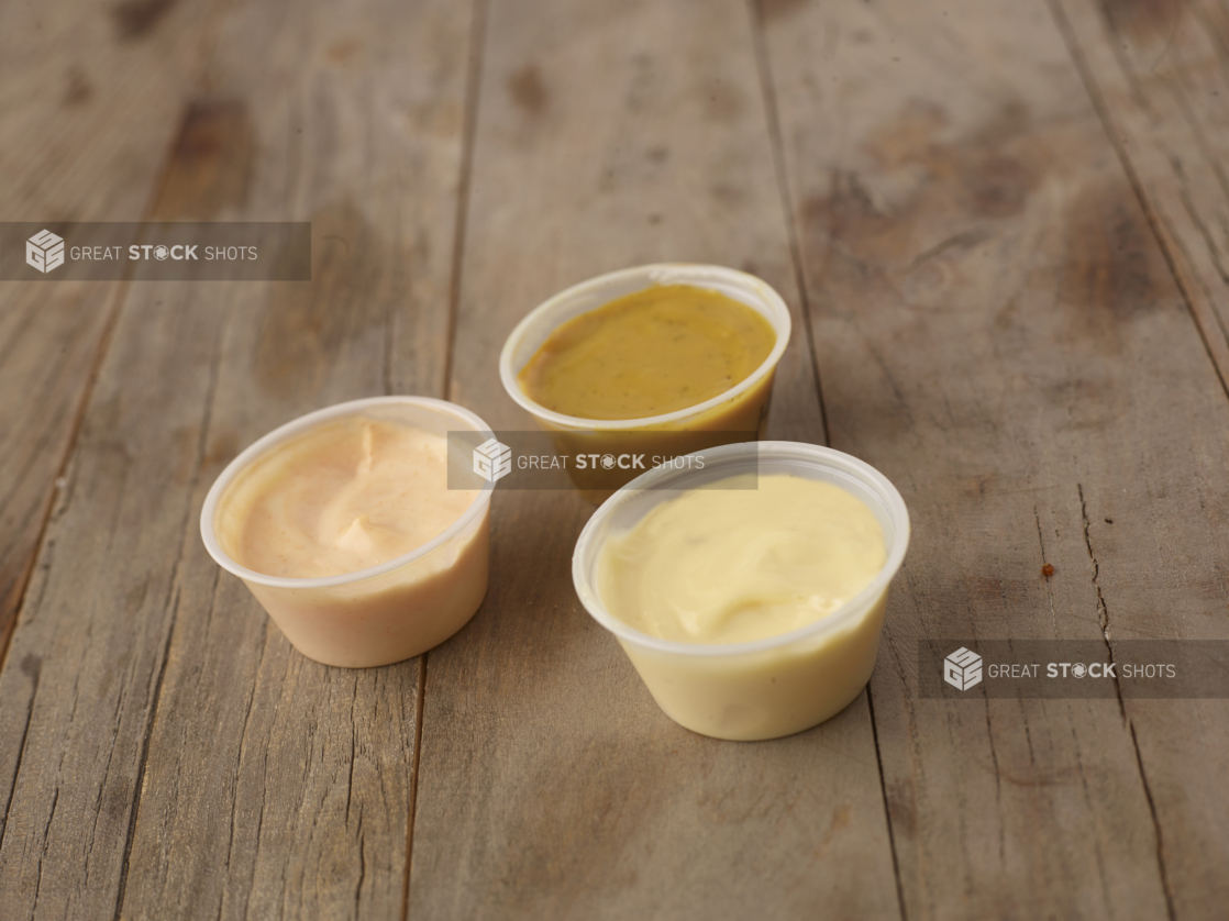 Close Up of a Trio of Dipping Sauces in Plastic Take-Out Container Cups on a Weathered Wooden Surface