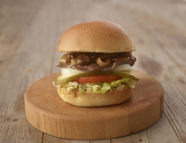 Close up of a Steak, Mushroom and Onion Burger with Fresh Vegetable Toppings on a Wooden Cutting Board on a Weathered Wood Surface
