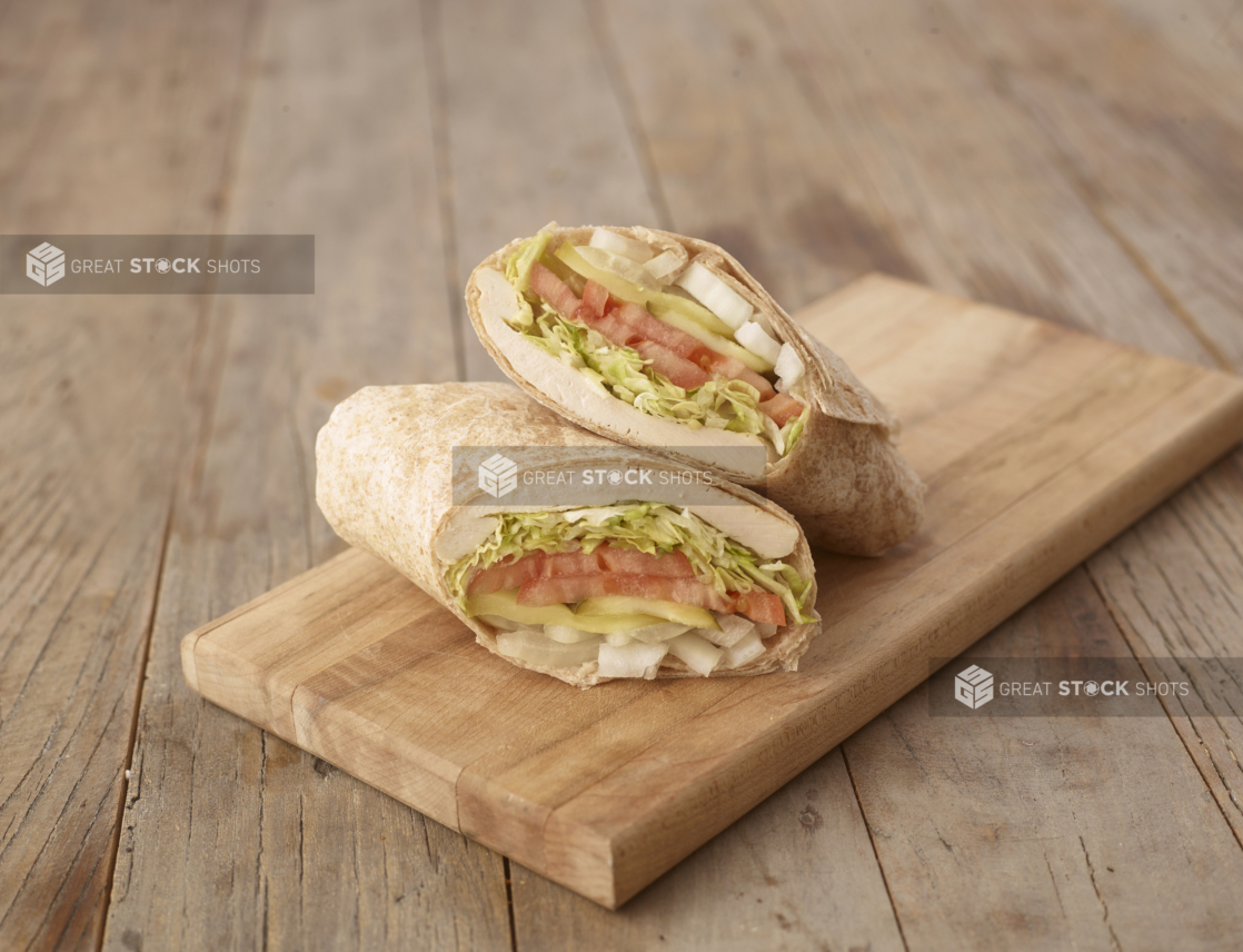 Close Up of a Cut Grilled Chicken Wrap with Fresh Vegetables on a Wooden Cutting Board on a Weathered Wooden Surface