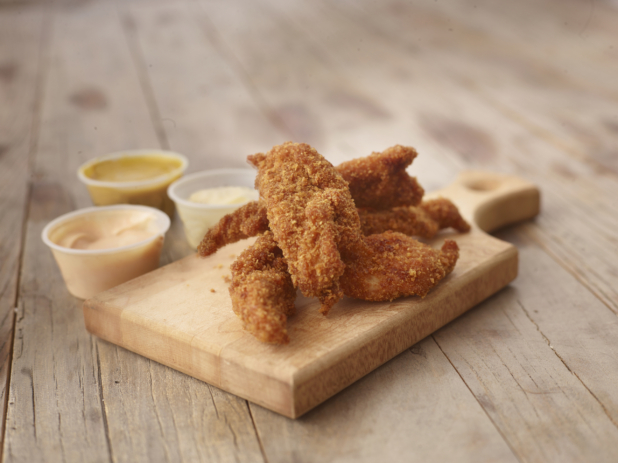 Deep Fried Breaded Chicken Tenders on a Wooden Cutting Board with a Trio of Dipping Sauces on a Weathered Wooden Surface