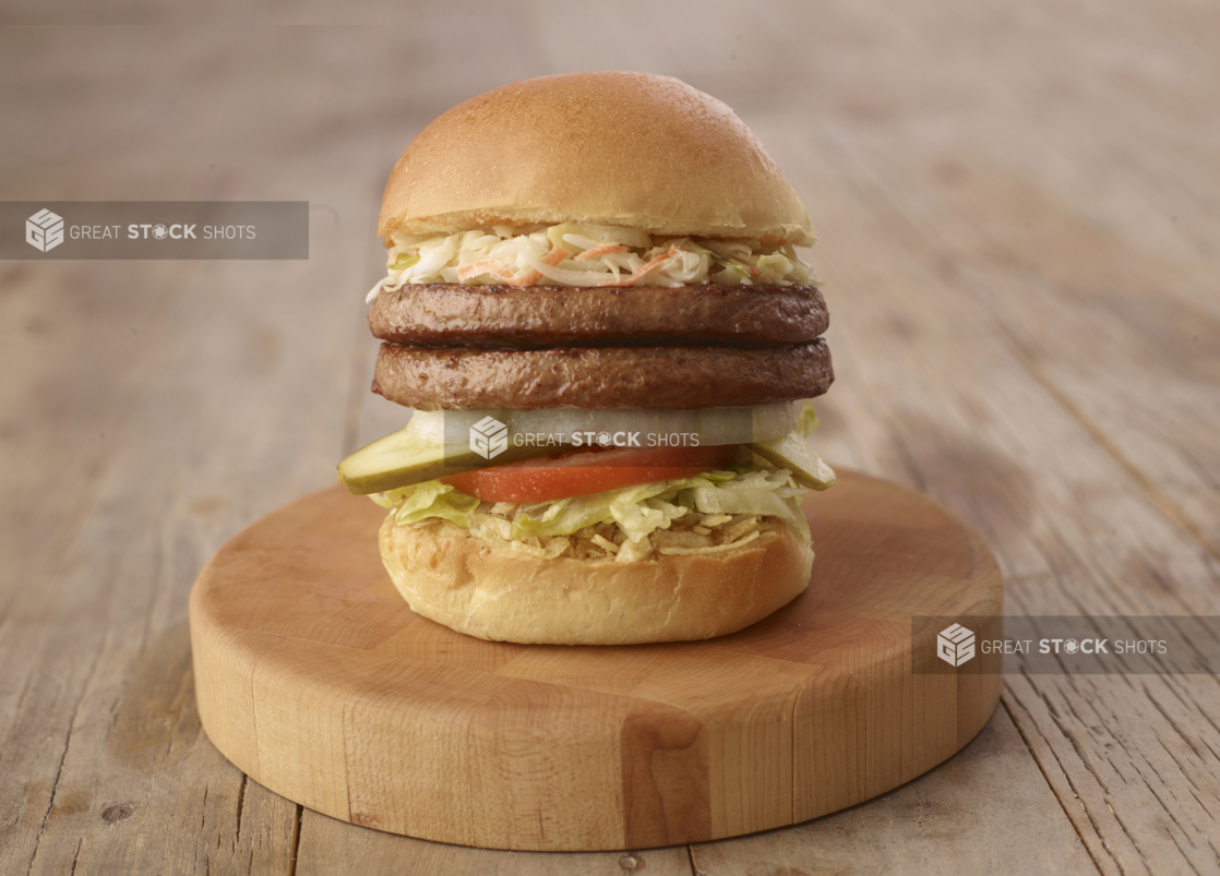 Close up of a Double Beef Patty Burger with Fresh Vegetable Toppings on a Wooden Cutting Board on a Weathered Wood Surface