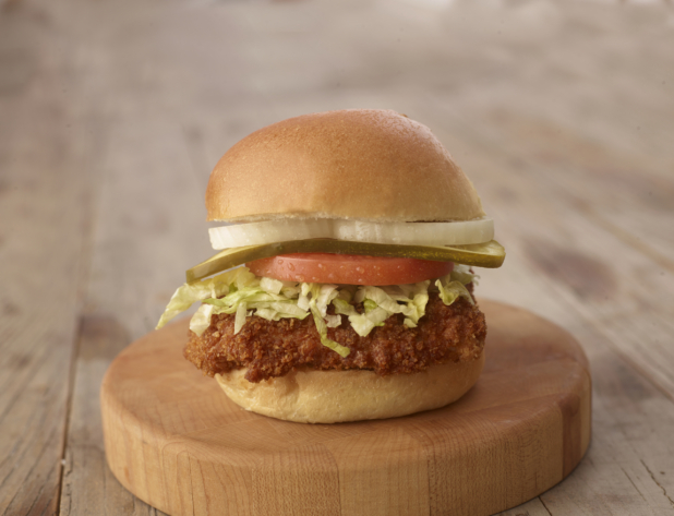 Close up of a Fried Chicken Sandwich with Fresh Vegetable Toppings on a Wooden Cutting Board on a Weathered Wood Surface