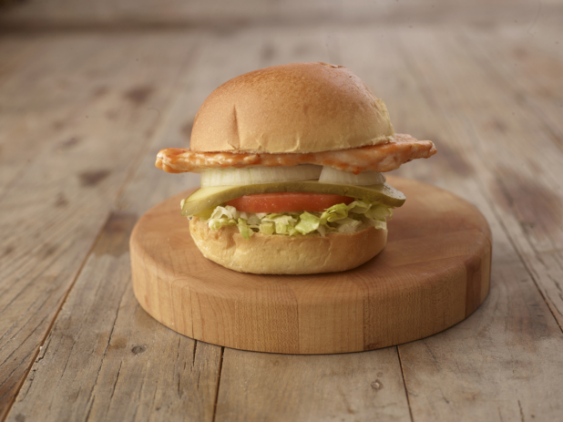 Close up of a Grilled Chicken Sandwich with Fresh Vegetable Toppings on a Wooden Cutting Board on a Weathered Wood Surface
