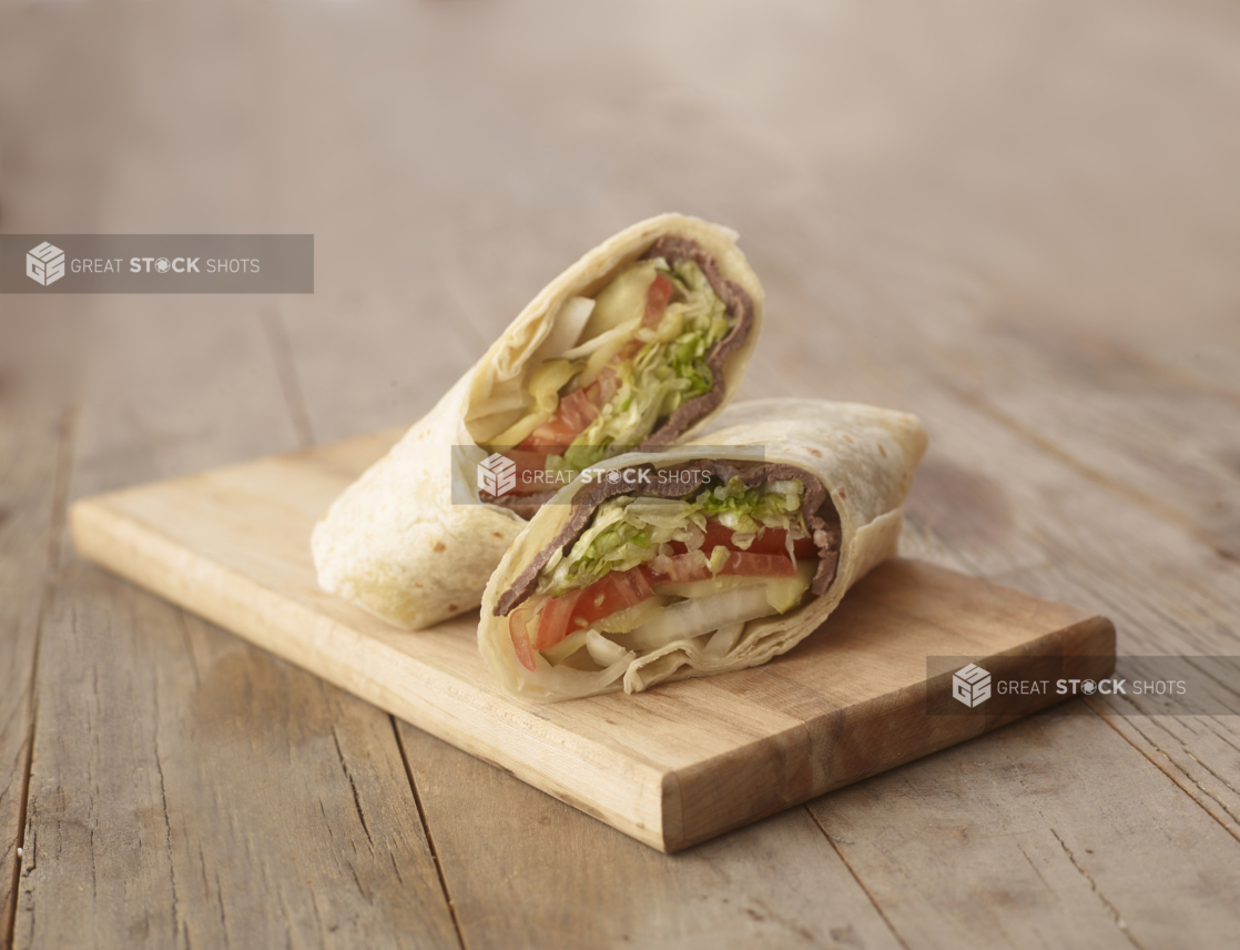 Close Up of a Cut Beef Steak Wrap with Fresh Vegetables on a Wooden Cutting Board on a Weathered Wooden Surface