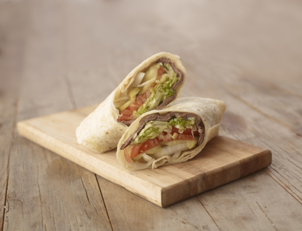 Close Up of a Cut Beef Steak Wrap with Fresh Vegetables on a Wooden Cutting Board on a Weathered Wooden Surface