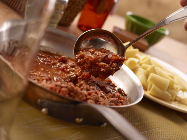 Hearty Homemade Bolognese Sauce in a Stainless Steel Skillet, Served with Rigatoni Pasta on a Wooden Surface in an Indoor Kitchen Setting