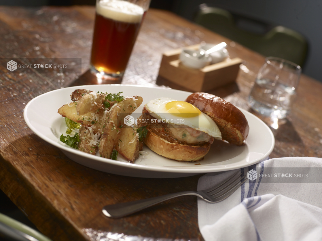 Turkey Burger Topped With a Fried Egg on a Grilled Potato Bun, Served with Parmesan Potato Wedges on a White Ceramic Dish