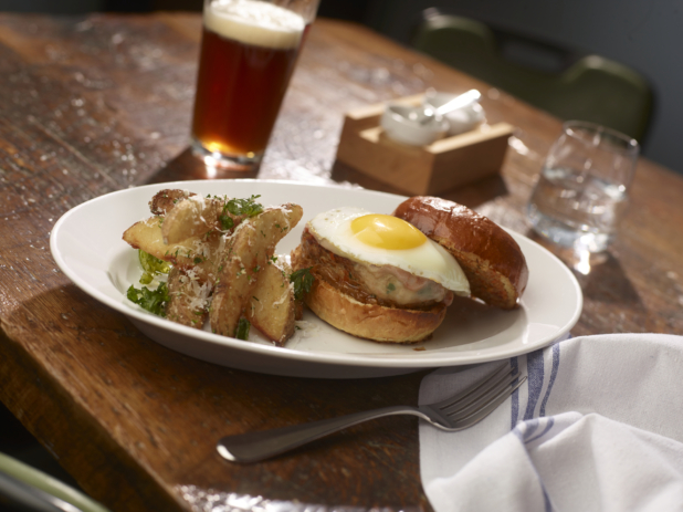 Turkey Burger Topped With a Fried Egg on a Grilled Potato Bun, Served with Parmesan Potato Wedges on a White Ceramic Dish