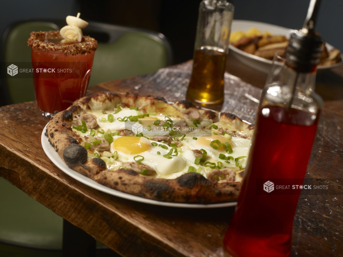 Neopolitan-Style Breakfast Pizza with Sunny Side Up Fried Eggs, Breakfast Sausage and Green Onions and a Caesar Cocktail in a Restaurant Setting