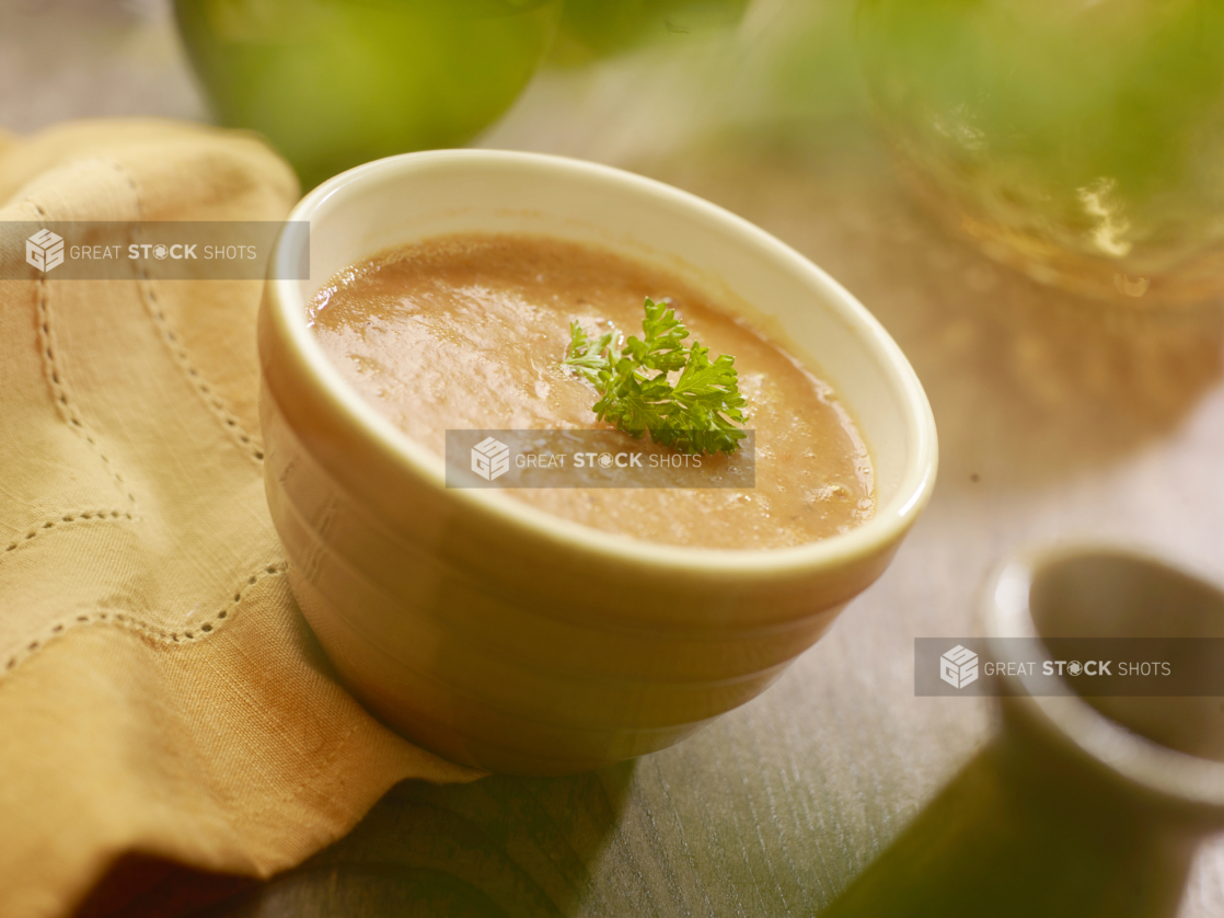 A Yellow Ceramic Bowl of Thick Carrot and Vegetable Soup with a Garnish of Fresh Parsley on a Wooden Table in an Indoor Setting